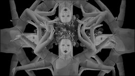 Black-and-white images of drag artist Maiden China are collaged over one another so that 4 images of the artists's face are in the center, with multiple arms emerging from each depiction. Maiden China wears an elaborate headpiece with a beaded veil extending in front of her face. She wears heavy white foundation, dark lipstick and a see-through mesh-top.
