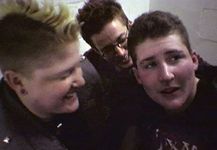 3 three white youth laughing in a corridor. One has a mohawk and the other two have short hair.