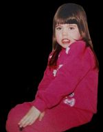 Childhood portrait of B.G-Osborne, about age 8.  They have straight brown hair with bangs, have light skin, and an expression of perhaps disgust or disinterest. They wear a red or pink tracksuit suggestive of the 80s or 90s.