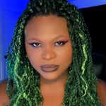 Kat Blaque with a neutral expression. She is a Black person with medium skin, long green twists, and elegant makeup with a cat eye.