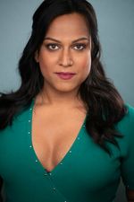 Aneesh Sheth is a transgender Indian-American woman with brown skin. She is posing in front of a light blue background with her hair pulled behind her ears and laying on her shoulders. She has a nose piercing and she is wearing a turquoise low cut blouse.