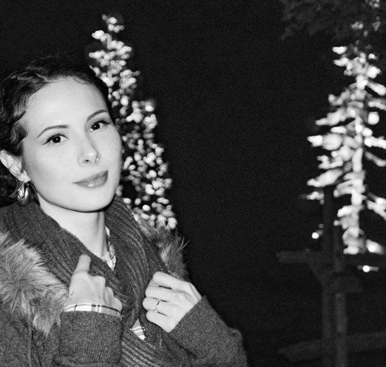 In this artful black-and-white photo, Neecha stands to the left of the frame, he hair pulled back. She smiles softly at the camera, he hands on the lapels of her fur-lined coat.